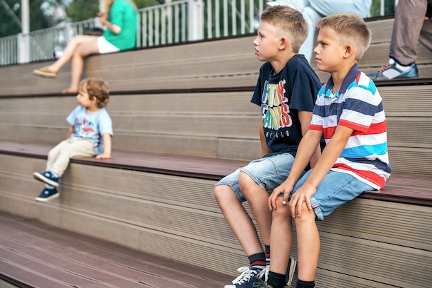 Ragazzi in eleganti abiti casual si siedono su una panca di legno guardando film su un enorme schermo nel parco pubblico