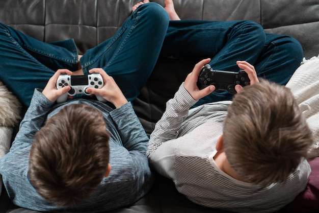 Ragazzi seduti sul divano con joystick di gioco dall'alto vista della corona e dell'occipite I bambini giocano ai videogiochi a casa