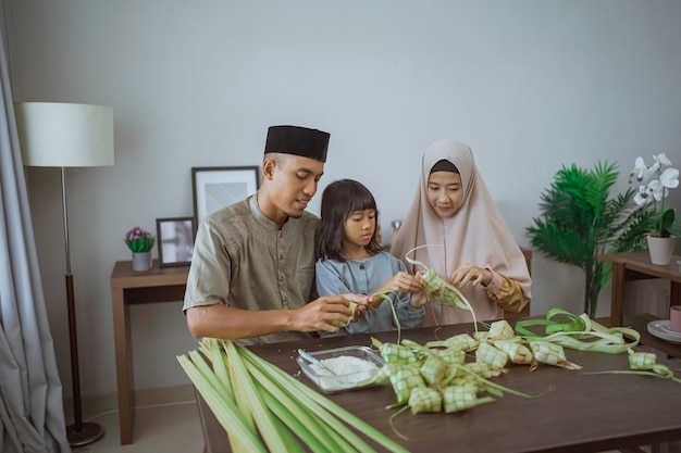 Ragazzina con i suoi genitori che preparano un ketupat a casa