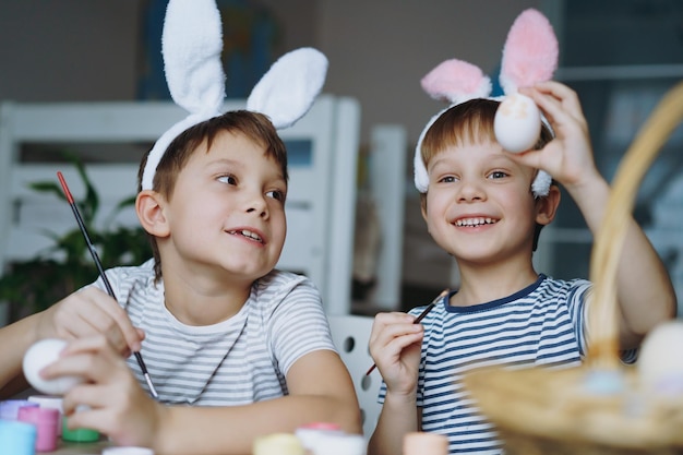 Ragazzini carini che indossano orecchie da coniglio che colorano le uova per Pasqua Immagine con fuoco selettivo