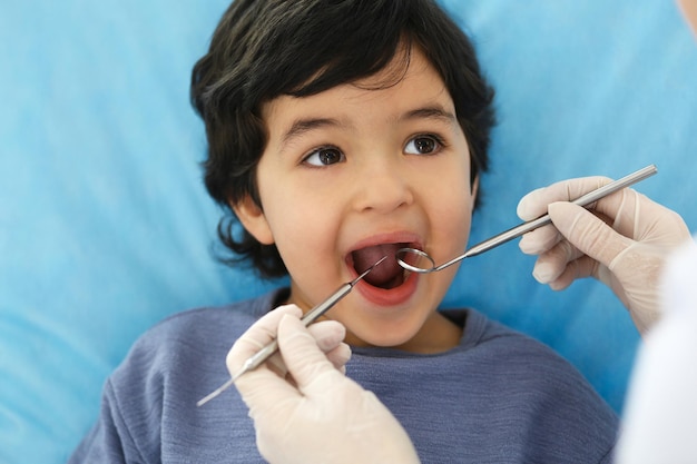 Ragazzino arabo seduto alla poltrona del dentista con la bocca aperta durante il controllo orale mentre il medico visita l'ufficio del dentista Concetto di medicina e stomatologia