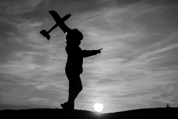 Ragazzino aviatore sopra il cielo al tramonto Il ragazzo sogna di diventare un pilota carino bambino che cammina nel grano