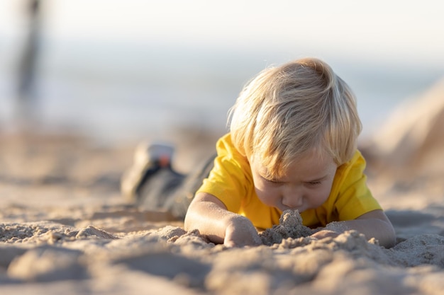 Ragazzino biondo sdraiato sulla sabbia sulla spiaggia