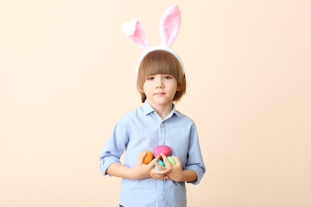 Ragazzino carino con le uova di Pasqua in mano e orecchie da coniglio in testa