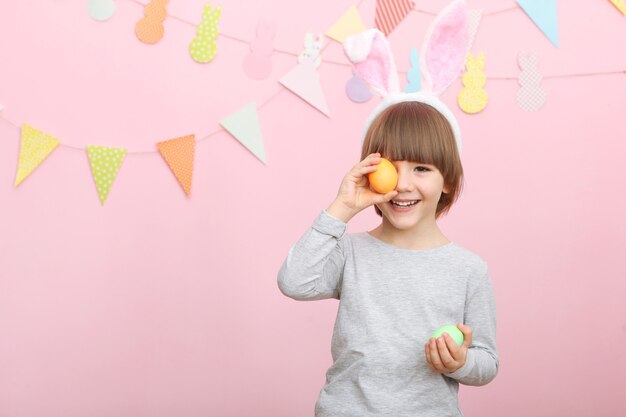 Ragazzino carino con le uova di Pasqua in mano e orecchie da coniglio in testa