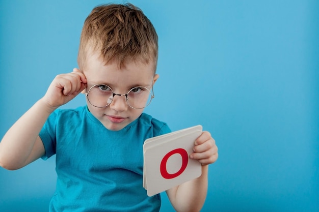 Ragazzino carino con lettera su sfondo blu Bambino che impara un alfabeto di lettere