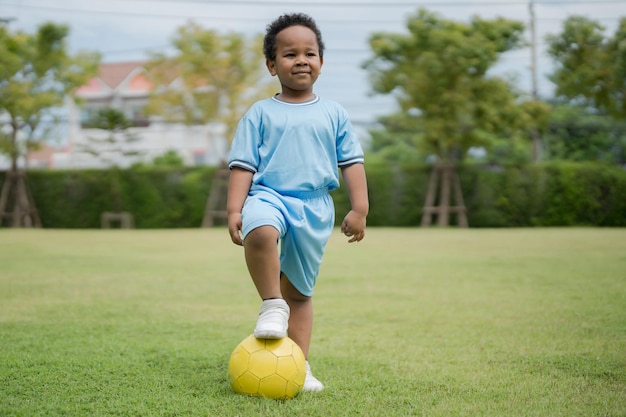 Ragazzino carino con pallone da calcio nel parco in una giornata di sole