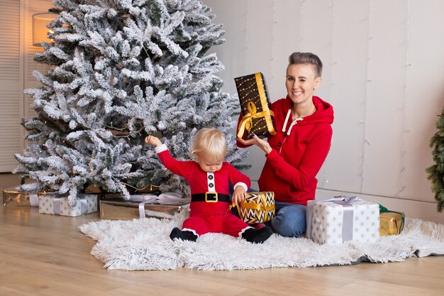 Ragazzino carino e madre che giocano con i regali vicino all'albero di Natale