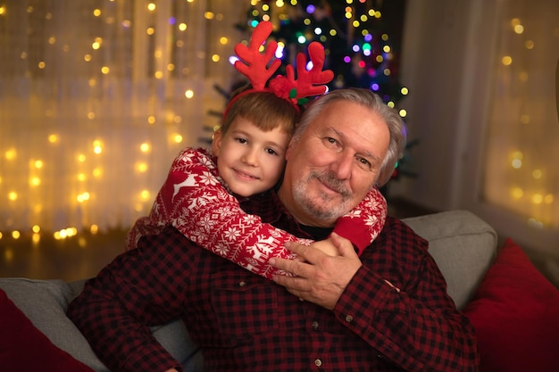 Ragazzino caucasico che abbraccia il nonno anziano in casa a Natale. Generazione familiare e amore.