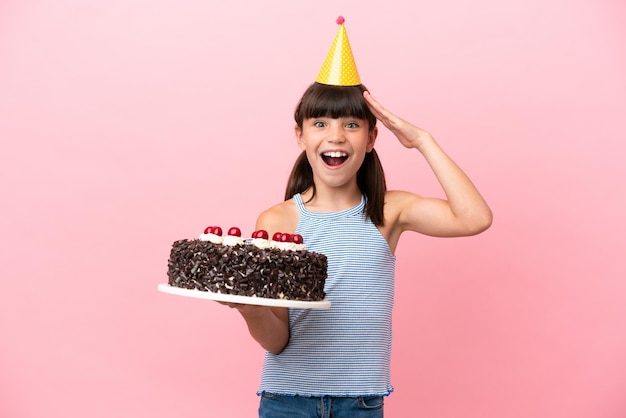 Ragazzino caucasico che tiene la torta di compleanno isolata su sfondo rosa con espressione a sorpresa