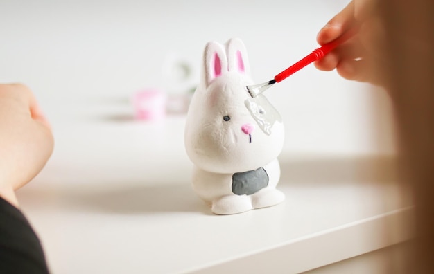 Ragazzino che dipinge la figura del coniglietto di pasqua in ceramica Bambino che fa artigianato fai-da-te Workshop