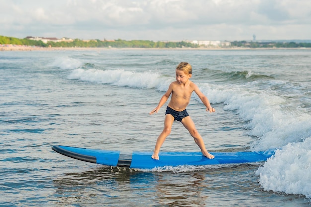 Ragazzino che fa surf su una spiaggia tropicale Bambino sulla tavola da surf sull'onda dell'oceano Sport acquatici attivi per bambini Nuoto per bambini con surf Lezione di surf per bambini