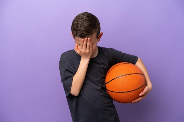 Ragazzino che gioca a basket isolato su sfondo viola con espressione stanca e malata