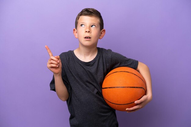 Ragazzino che gioca a basket isolato su sfondo viola pensando un'idea che punta il dito verso l'alto