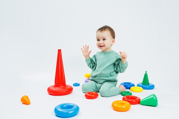 Ragazzino che gioca a giochi educativi logici con piramide di plastica isolata su sfondo bianco Un bambino felice gioca con un giocattolo educativo Il bambino ha un anno e quattro mesi