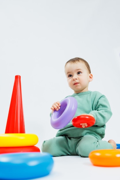 Ragazzino che gioca a giochi educativi logici con piramide di plastica isolata su sfondo bianco Un bambino felice gioca con un giocattolo educativo Il bambino ha un anno e quattro mesi