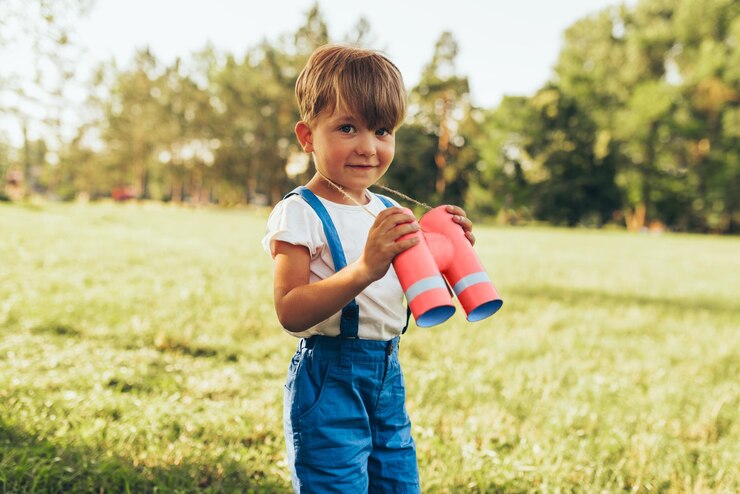 Ragazzino che gioca con un binocolo alla ricerca di un'immaginazione o di un'esplorazione in una giornata estiva nel parco Bambino felice che gioca finta safari all'aperto nella foresta Concetto di infanzia