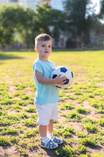 Ragazzino che gioca con un pallone da calcio sul campo di estate