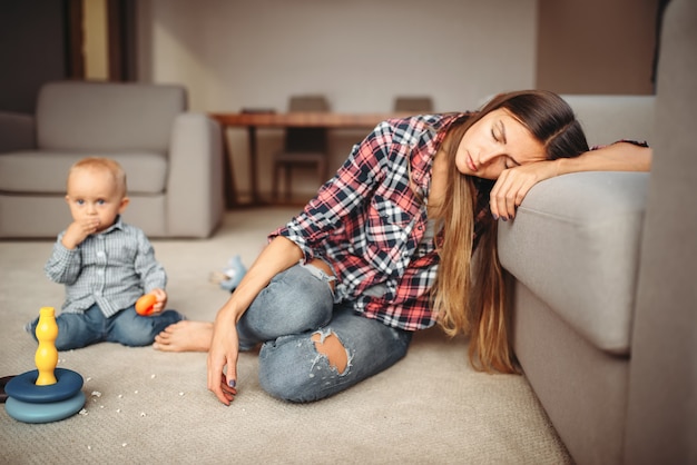 Ragazzino che gioca sul pavimento, la madre dorme