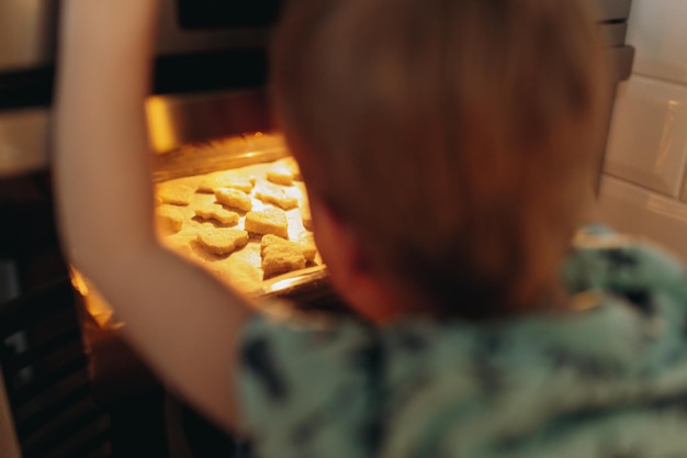 Ragazzino che guarda attraverso il vetro nel forno dove cuociono i biscotti. Concetto di vacanza di Natale. Immagine con messa a fuoco selettiva