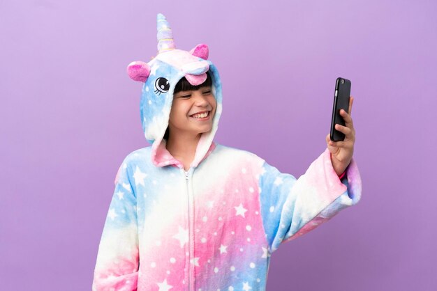 Ragazzino che indossa un pigiama unicorno isolato su sfondo viola che fa un selfie