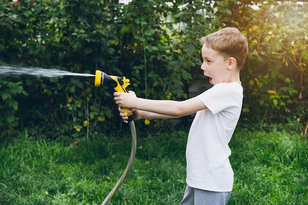 Ragazzino che innaffia il giardino con un tubo flessibile.