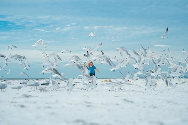 Ragazzino che insegue gli uccelli vicino alla spiaggia del mare estivo bambino felice che gioca con gli uccelli gabbiano fuori in estate