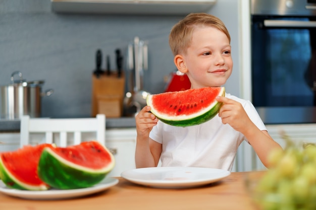 Ragazzino che mangia pezzo di anguria in cucina