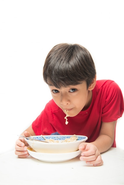 Ragazzino che mangia spaghetti istantanei su bianco