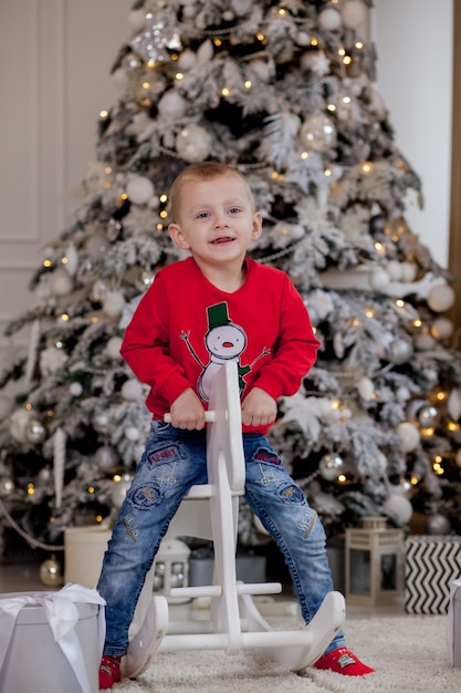 Ragazzino che monta un cavallo di cartone vicino all'albero di Natale