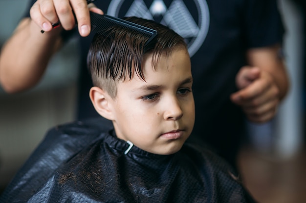 Ragazzino che ottiene taglio di capelli dal barbiere mentre sedendosi nella sedia al barbiere.