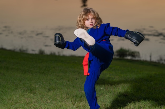 Ragazzino che pratica box sport all'aria aperta karate bambini ragazzino in kimono che fa box nel parco bambino con b