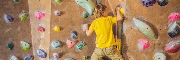 Ragazzino che si arrampica su una parete rocciosa con stivali speciali banner per interni formato lungo