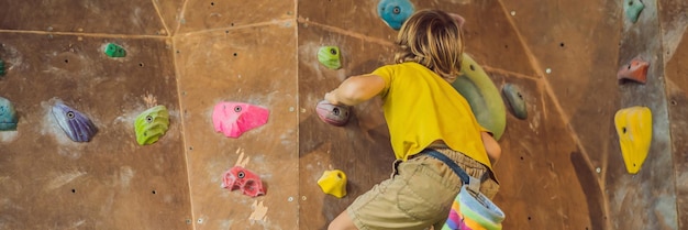 Ragazzino che si arrampica su una parete rocciosa con stivali speciali banner per interni formato lungo