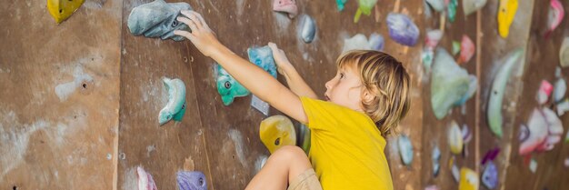 Ragazzino che si arrampica su una parete rocciosa con stivali speciali banner per interni formato lungo