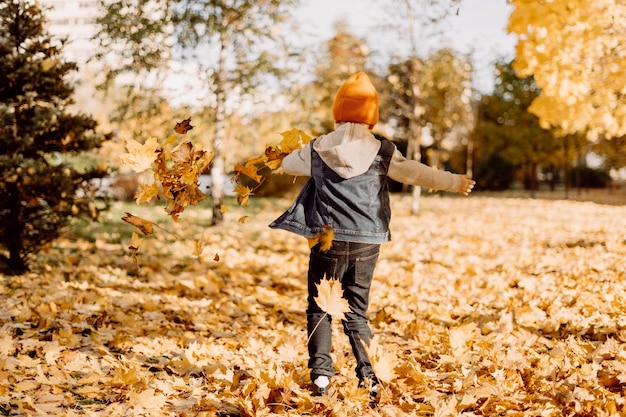 Ragazzino che si diverte nel parco autunnale con foglie cadute che vomitano all'aperto un ragazzo di foglie che gioca con