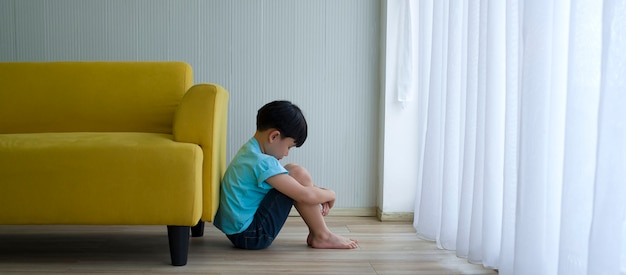 Ragazzino che si siede accanto al sofà giallo a casa. Autismo infantile.