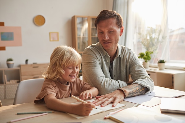 Ragazzino che studia con suo padre al tavolo suo padre aiutandolo con i compiti in camera