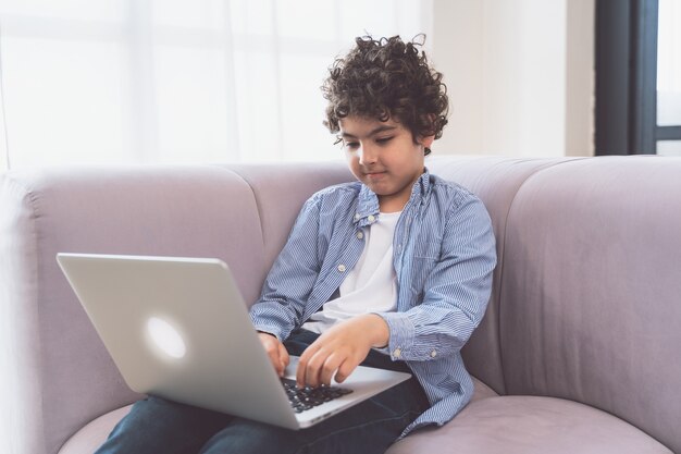 Ragazzino che studia sul suo computer portatile. Concetto di infanzia e tecnologia