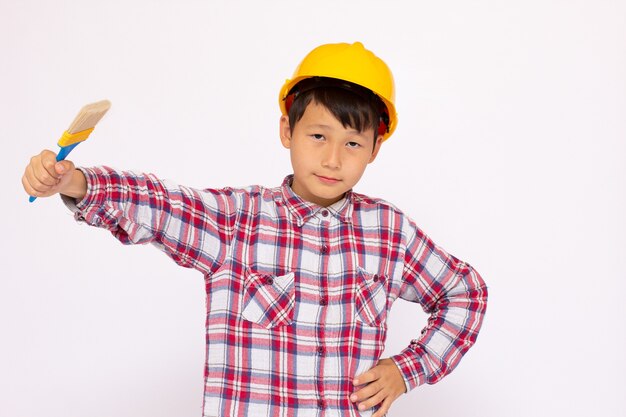 Ragazzino come operaio edile che indossa un casco giallo con un pennello in mano