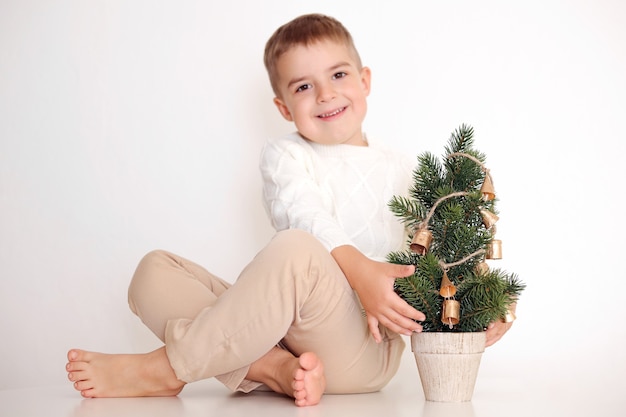 Ragazzino con albero di Natale su fondo bianco. Bambino felice, festa di Natale, tempo di Natale.