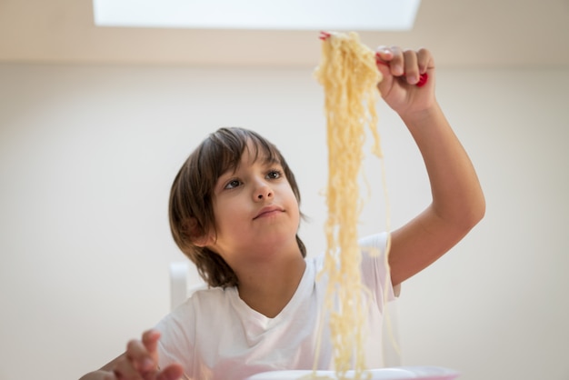 Ragazzino con capelli lunghi che mangia spaghetti