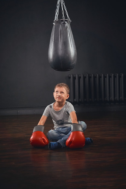 Ragazzino con guantoni da boxe seduto sul pavimento