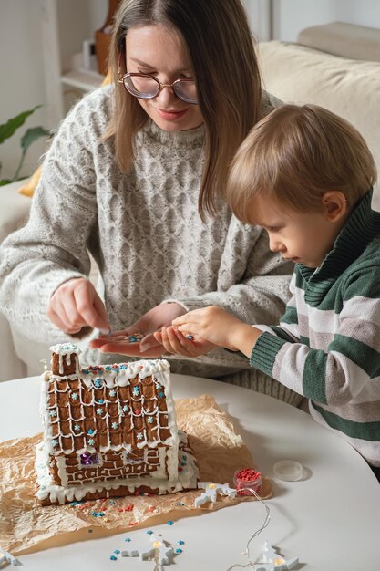 Ragazzino con la mamma che decora insieme la casa di pan di zenzero di Natale, attività familiari e tradizioni a Natale e Capodanno