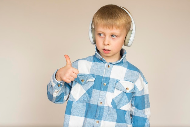 Ragazzino con le cuffie che ascolta musica e mostra i pollici su uno sfondo grigio