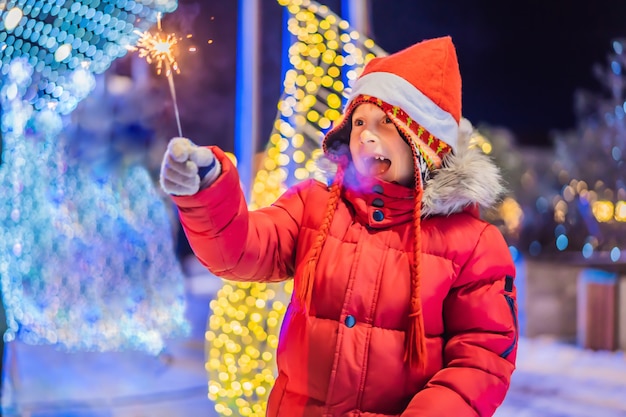 Ragazzino con stelle filanti vicino albero di abete gigante e sfondo di illuminazione di Natale