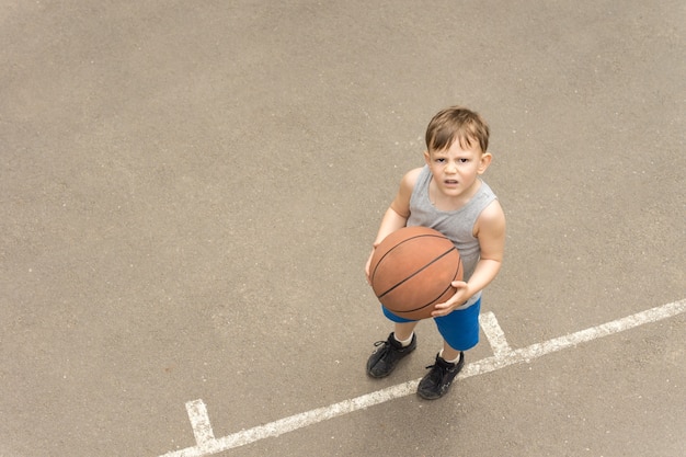 ragazzino con un pallone da basket in mano in piedi su un campo all'aperto