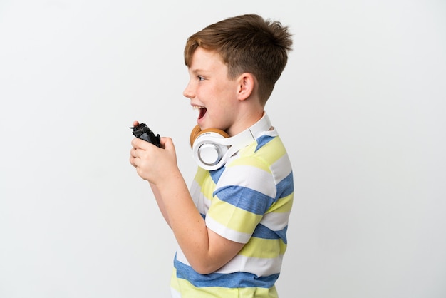 Ragazzino dai capelli rossi che tiene in mano un game pad isolato su sfondo bianco che ride in posizione laterale