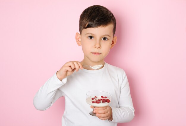 Ragazzino di 6 anni che mangia yogurt con bacche rosse su una superficie rosa