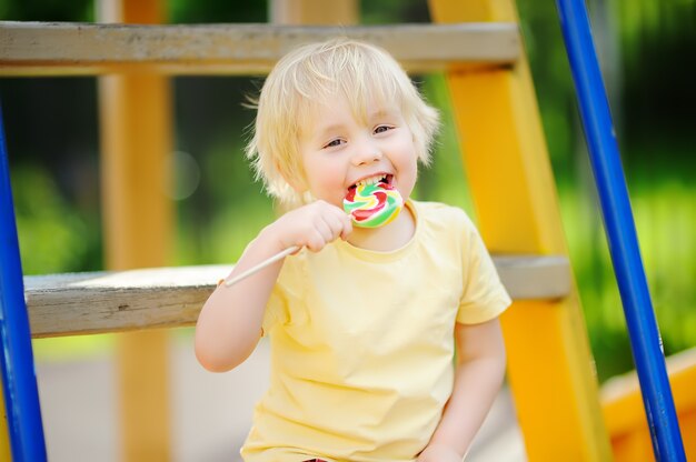 Ragazzino divertendosi e mangiando grande lecca-lecca sul parco giochi all&#39;aperto